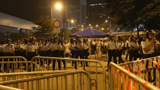 Eine Reihe von Polizisten in Uniform stehen hinter einer Absperrung in der Nacht.