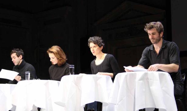 Vier Schauspieler sitzen an Tischen mit weißen Tischdecken und lesen aus ihren Skripten.