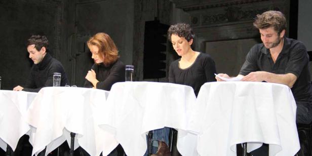 Vier Personen sitzen an einem Tisch mit weißen Tischdecken und lesen Papiere.