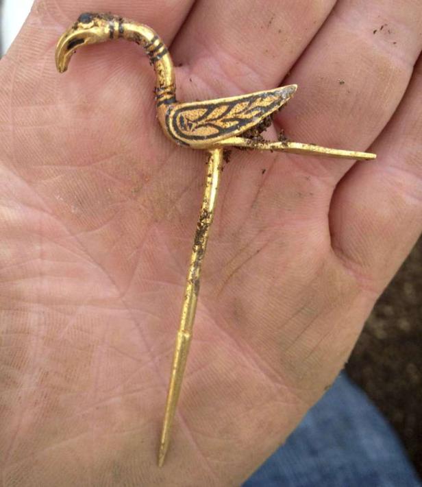 Eine goldene, vogelartige Brosche liegt in einer Hand.