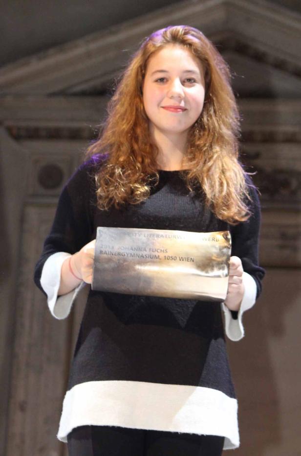 Eine junge Frau hält eine Auszeichnung mit der Aufschrift „Johanna Fuchs, Rainergymnasium, 1050 Wien“.