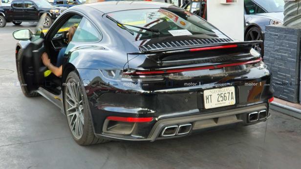 Ein schwarzer Porsche 911 mit geöffneter Fahrertür an einer Tankstelle.
