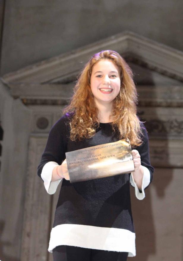 Johanna Fuchs, eine junge Frau, hält eine Auszeichnung des Rainergymnasiums, 1050 Wien, in den Händen.