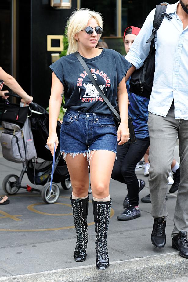 Lady Gaga mit blonden Haaren, Sonnenbrille, T-Shirt und Stiefeln auf der Straße.