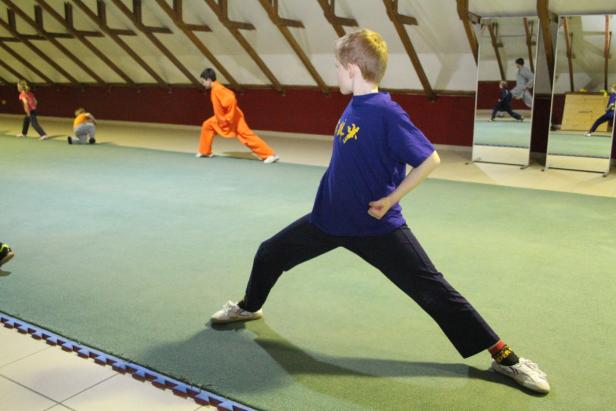 Eine Gruppe von Kindern trainiert Kung Fu in einer Turnhalle.