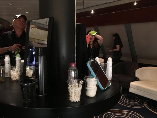 Auf einem runden Tisch stehen Kosmetikartikel und Spiegel, im Hintergrund sind Personen zu sehen.