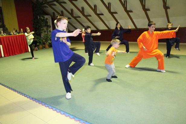 Eine Gruppe von Kindern und Erwachsenen übt Kung Fu in einem Raum.