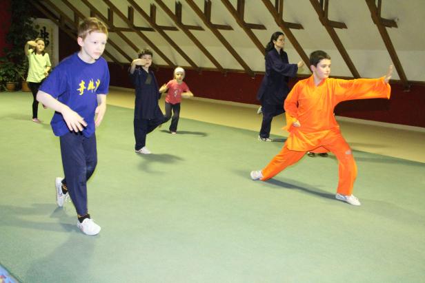 Eine Gruppe von Kindern und Erwachsenen übt Kung Fu in einem Raum.