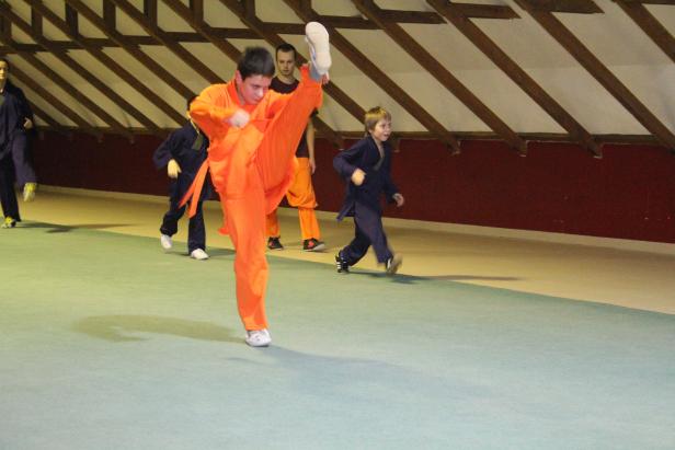 Ein junger Mann im orangefarbenen Kampfanzug macht einen hohen Tritt während des Trainings.