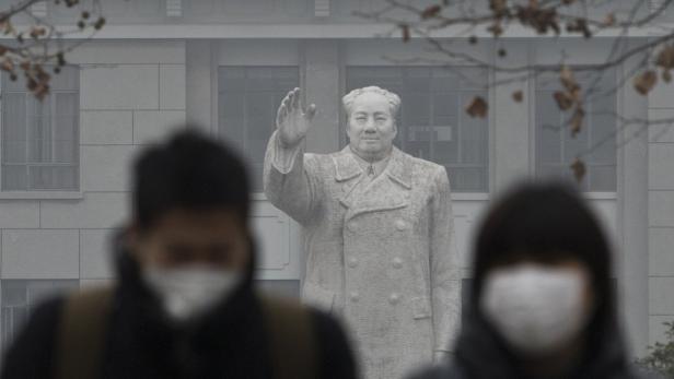 Eine Statue von Mao Zedong vor einem Gebäude, mit verschwommenen Personen im Vordergrund.