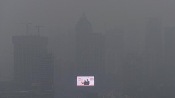 Dichte Smogwolken verdecken eine Stadtlandschaft mit Hochhäusern und einem Werbeplakat.