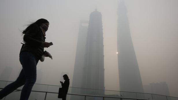 Menschen mit Gesichtsmasken gehen in Shanghai an Hochhäusern im Nebel vorbei.