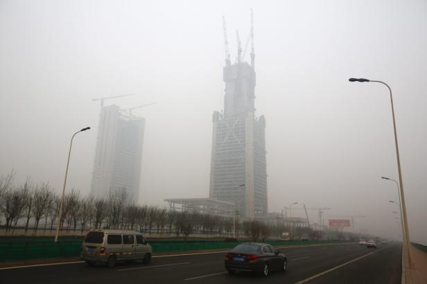 Im Nebel sind Hochhäuser im Bau zu sehen, während Autos auf der Straße fahren.