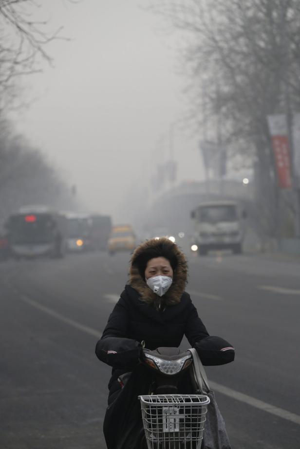 Eine Frau mit Atemschutzmaske fährt auf einem Moped durch dichten Smog.