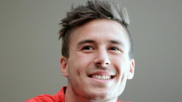 Ein lächelnder junger Mann mit braunen Augen und gestylten Haaren.