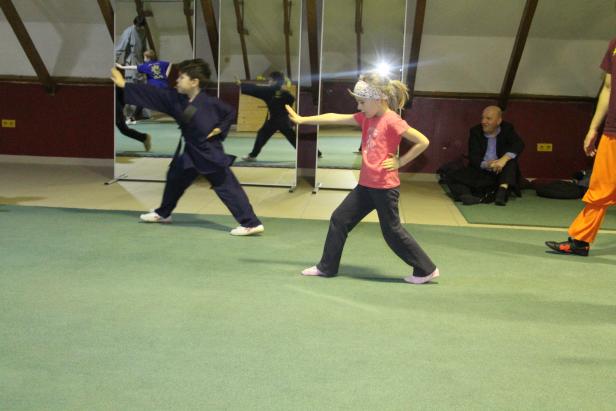 Kinder üben Kampfsportarten in einer Turnhalle vor einem Spiegel.