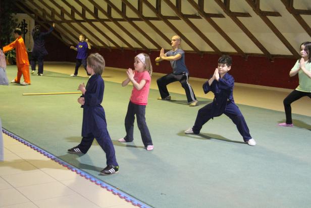 Eine Gruppe von Kindern und ein Erwachsener üben Kampfsport in einer Halle.