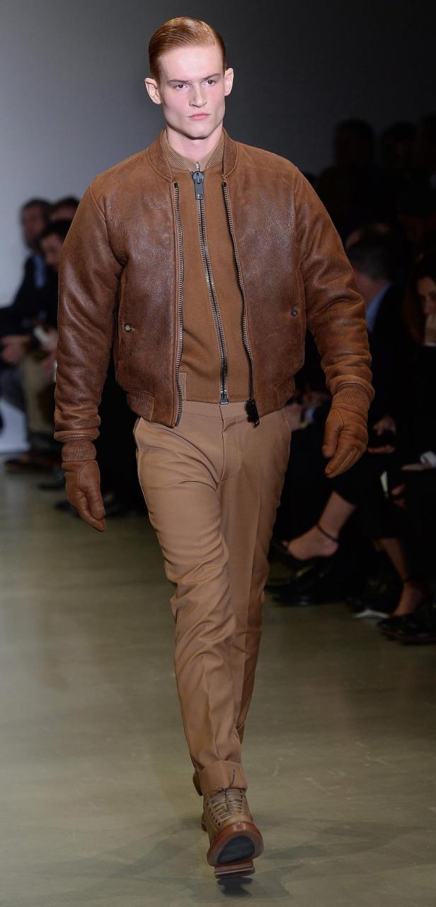 Ein Mann in brauner Lederjacke und passender Hose läuft auf einem Laufsteg.