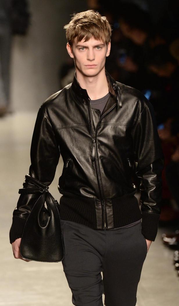 Ein Mann in einer schwarzen Lederjacke und Hose mit einer schwarzen Handtasche.