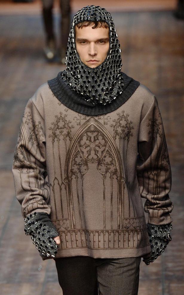 Ein Mann trägt ein mittelalterlich inspiriertes Outfit mit Kettenhemd-Kapuze und gotischem Muster.