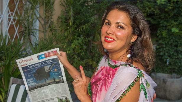 Grillfest bei Anna Netrebko und Yusif Eyvazov im G… Eine Frau liest im Garten eine Zeitung mit dem Titel „Sternenregen im August“.