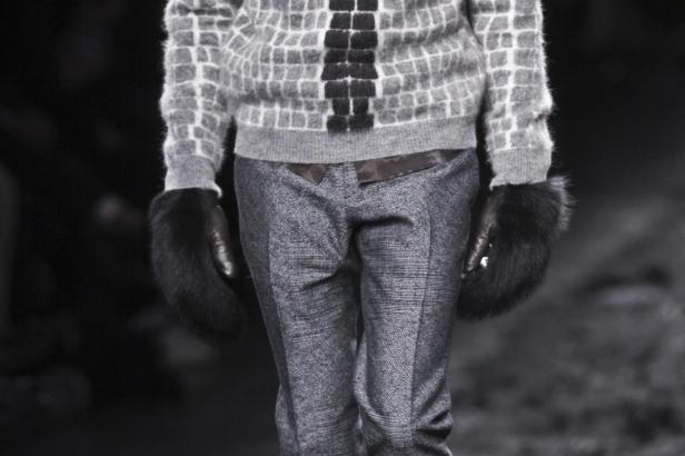 Eine Person trägt einen grauen Pullover, eine graue Hose und Pelzhandschuhe.