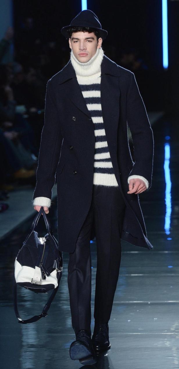 Ein Mann in einem dunklen Mantel und einem gestreiften Pullover trägt eine Tasche.