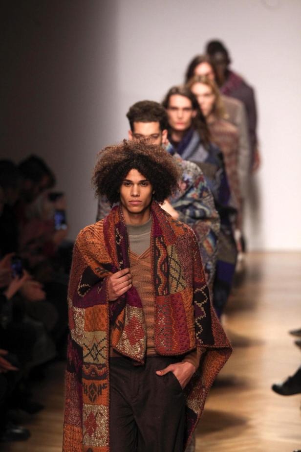 Ein Mann mit Afro und einem bunten Poncho läuft auf einem Laufsteg.