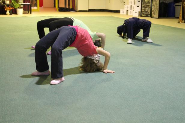 Drei Personen machen auf einem grünen Teppichboden eine Rückwärtsbeuge.