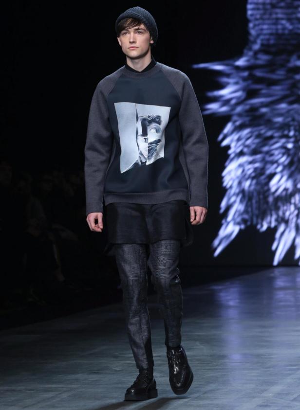 Ein Mann auf dem Laufsteg trägt einen Pullover mit einem grafischen Aufdruck.