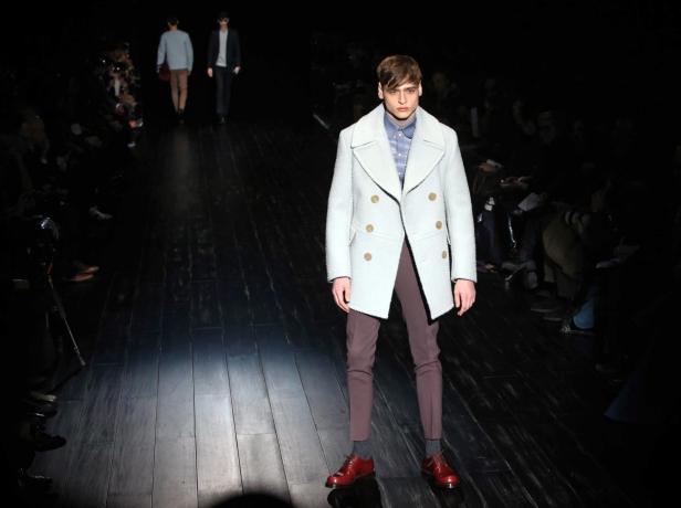 Ein Mann in einem hellblauen Mantel und braunen Hosen auf einem Laufsteg.