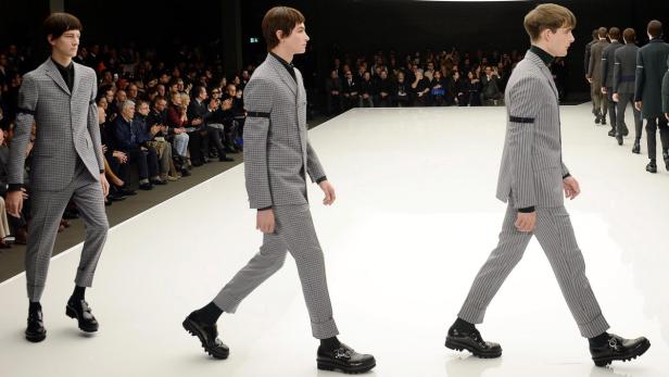 Männliche Models präsentieren Anzüge auf einem Laufsteg vor Publikum.