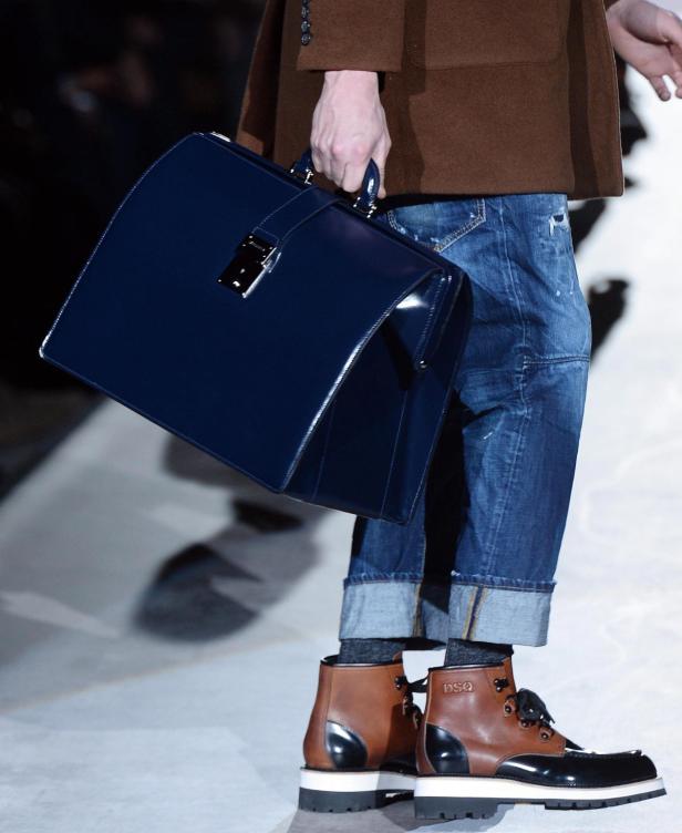 Ein Mann trägt eine blaue Aktentasche, Jeans und braune Stiefel.