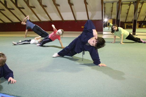 Eine Gruppe von Kindern und Erwachsenen übt gemeinsam eine Sportart in einem Raum.