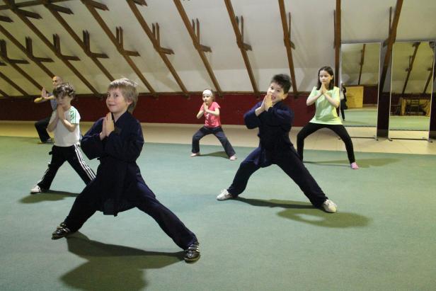 Eine Gruppe Kinder übt eine Kampfkunst in einem Raum mit Spiegeln.