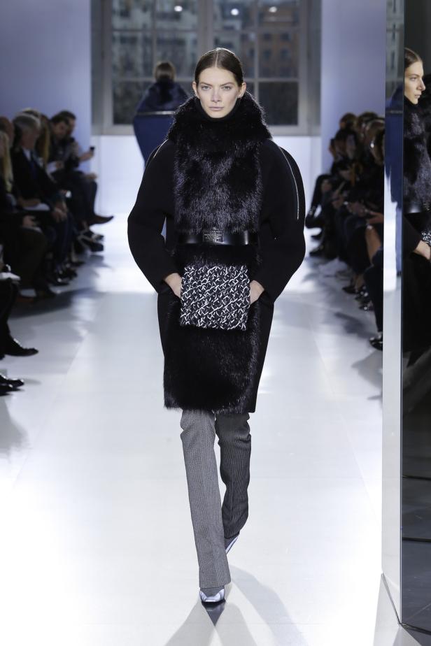 Eine Frau in einem schwarzen Mantel mit Pelzkragen auf einem Laufsteg.