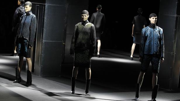 Models präsentieren Mode auf einem Laufsteg mit dunklem Hintergrund.