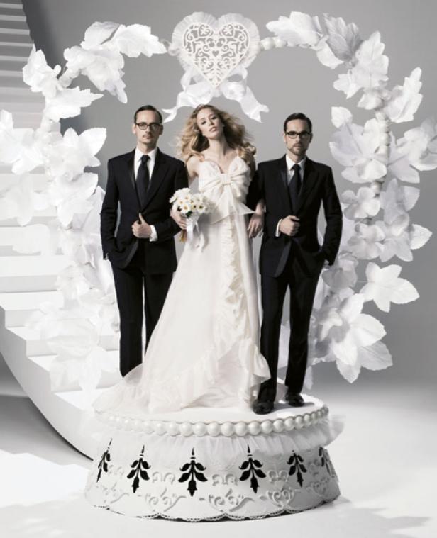 Eine Braut steht mit zwei Männern in Anzügen auf einer verzierten Hochzeitstorte.