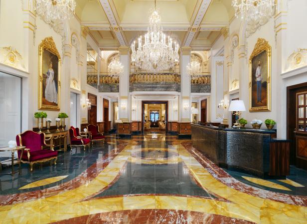 Die Lobby eines eleganten Hotels mit Marmorboden, Kronleuchtern und Porträtgemälden.