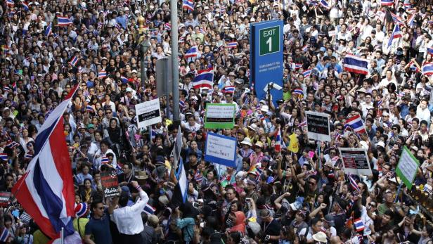 Eine große Menschenmenge schwenkt thailändische Flaggen und hält Schilder bei einer Demonstration.