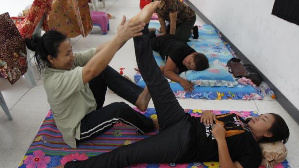 Eine Frau dehnt das Bein einer anderen Frau, die auf einer Matte liegt.