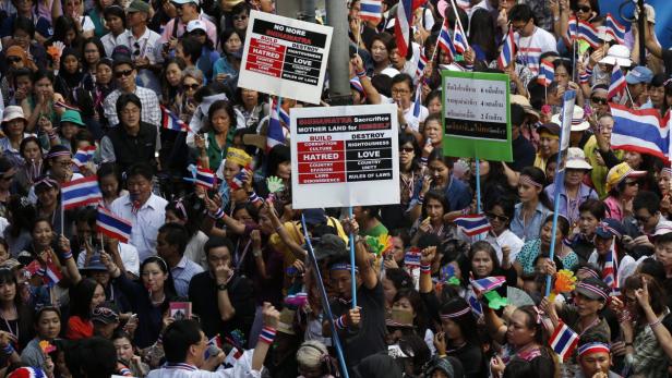 Eine Menschenmenge demonstriert mit thailändischen Flaggen und Schildern gegen Shinawatra.