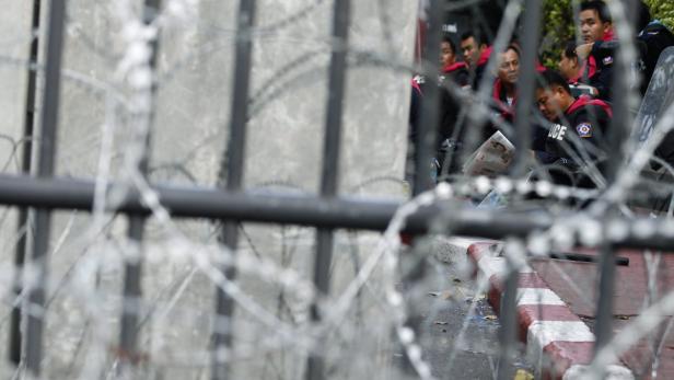 Polizisten sitzen hinter einem Zaun mit Stacheldraht und lesen Zeitung.