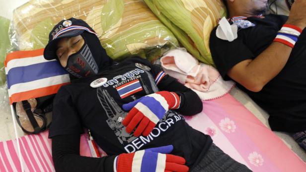 Ein Demonstrant mit thailändischer Flagge schläft, mit „Demokratie“-Handschuhen bedeckt.