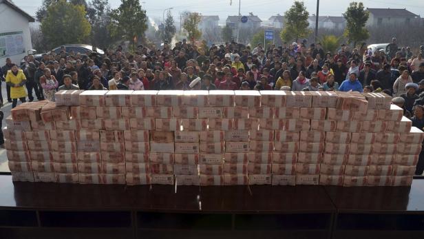 Eine große Menschenmenge steht hinter einem Tisch mit einem Stapel chinesischer Yuan-Bündel.