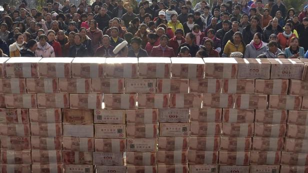Eine Menschenmenge steht hinter einer Mauer aus Geldbündeln.