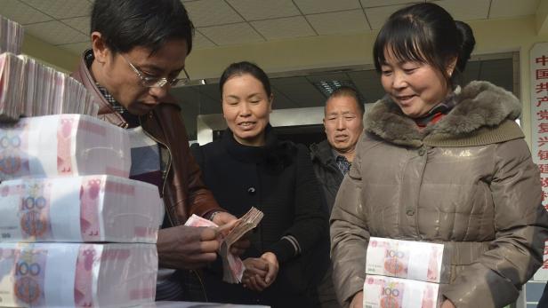 Mehrere Personen hantieren mit Bündeln von 100-Yuan-Banknoten.