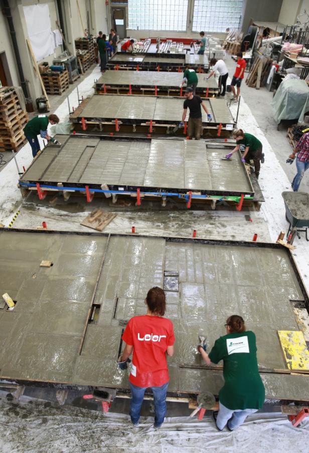 Mehrere Personen arbeiten an großen Betonplatten in einer Werkshalle.