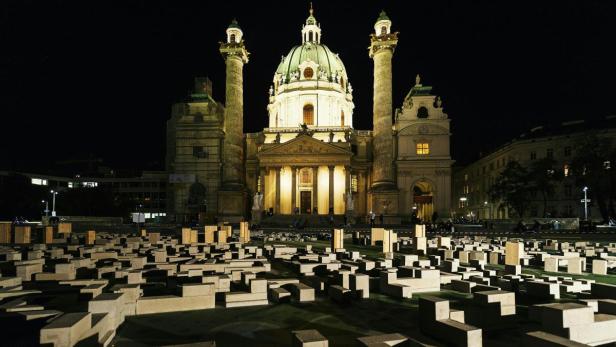 Die Karlskirche in Wien ist nachts hell erleuchtet, im Vordergrund eine Installation aus Betonblöcken.