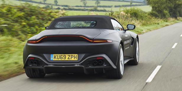 Ein mattschwarzer Aston Martin Vantage Roadster fährt auf einer Landstraße.